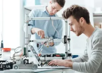 A man working on his laptop on a table while another men working behind